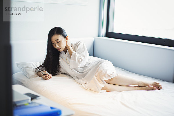 Eine Frau im Bett in einem Hotel  die ihr Smartphone benutzt.