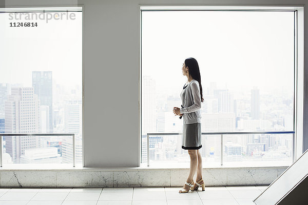 Eine Geschäftsfrau in einem Kleid am Fenster mit Blick auf eine Stadt
