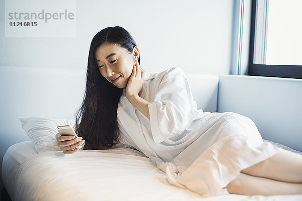 Eine Geschäftsfrau  die sich auf die Arbeit vorbereitet  aufwacht und ihr Smartphone im Bett überprüft.