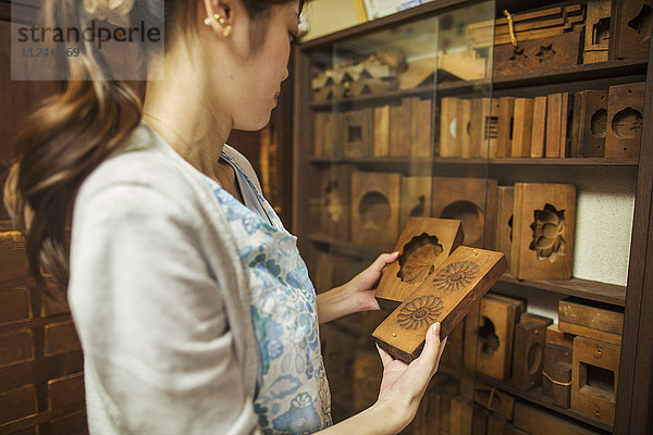 Ein kleiner handwerklicher Hersteller von speziellen Leckereien  Süßigkeiten namens Wagashi. Eine Frau hält geformte Holzformen in der Hand  die bei der Herstellung von Süßigkeiten verwendet werden.