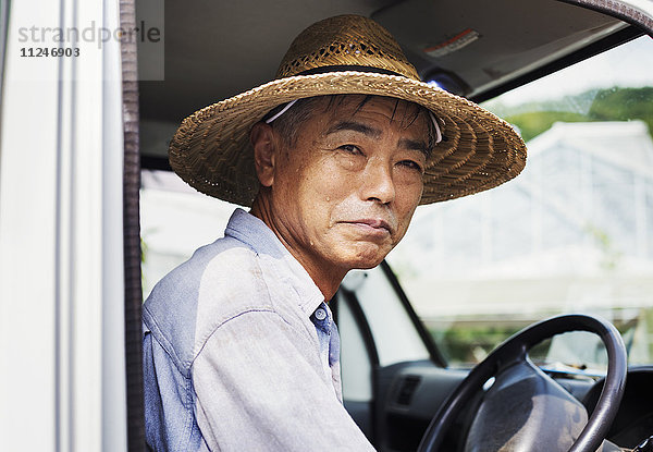 Ein Mann mit Hut  der auf dem Fahrersitz eines Lastwagens sitzt.