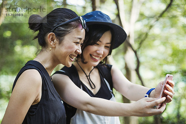 Zwei junge Frauen  die in einem Wald stehen und sich ein Selfie nehmen.