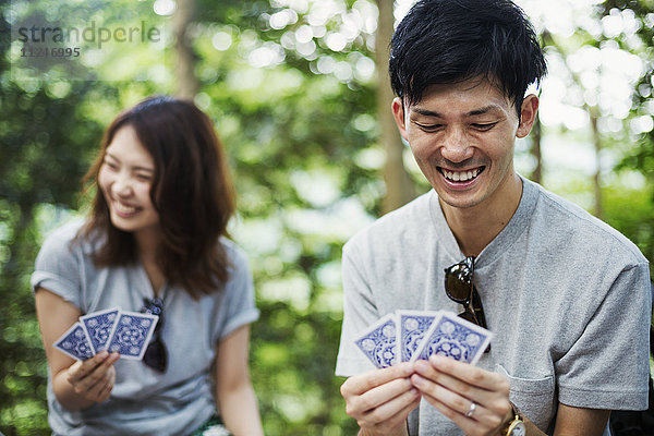 Junge Frau und Mann sitzen in einem Wald und spielen Karten.