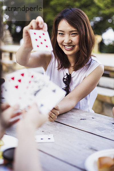 Lächelnde junge Frau  die an einem Tisch sitzt und Karten spielt.