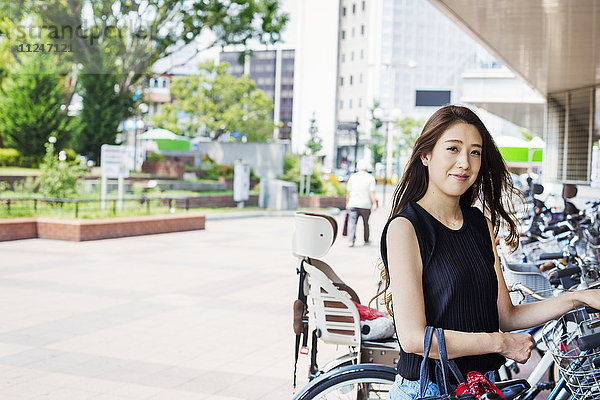 Lächelnde junge Frau mit langen braunen Haaren steht neben einem Fahrrad.