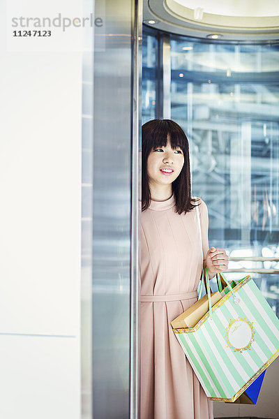 Junge Frau mit langen braunen Haaren in einem Einkaufszentrum  die Einkaufstaschen trägt.