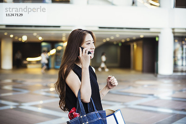 Junge Frau mit langen braunen Haaren in einem Einkaufszentrum  am Telefon.