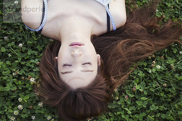 Junge Frau mit langen braunen Haaren auf einem Rasen liegend.