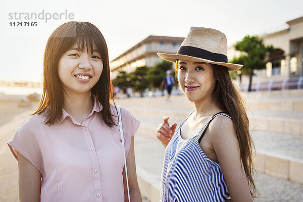 Zwei junge Frauen mit langen braunen Haaren vor einem Einkaufszentrum.