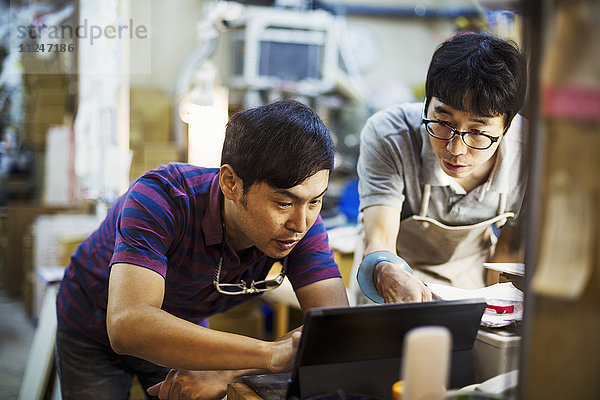 Zwei Männer mit einem Laptop-Computer  die zusammen in einer Glasmacherwerkstatt arbeiten.