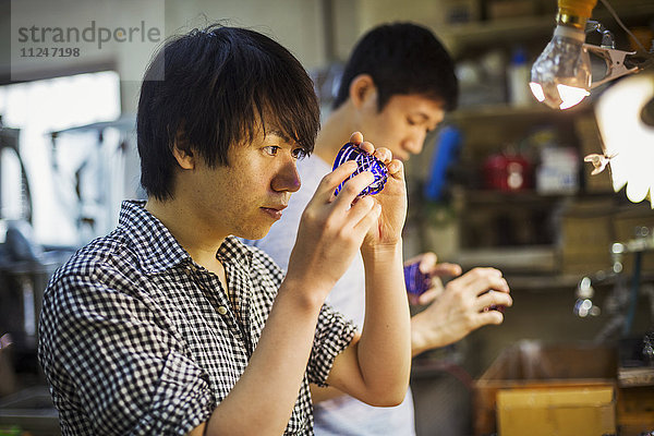 Ein Handwerker bei der Arbeit in der Werkstatt eines Glasmachers  der an einem lebhaft blau geschliffenen Glasobjekt arbeitet.