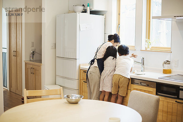 Familienhaus. Eine Mutter und zwei Kinder stehen an der Spüle in einer Küche.