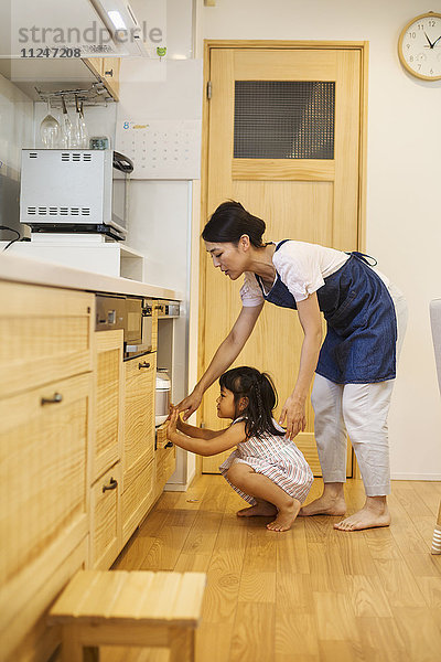 Familienhaus. Eine Frau und ein Mädchen bücken sich  um in einen Ofen zu schauen.