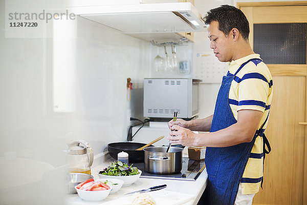 Familienhaus. Ein Mann in einer blauen Schürze bei der Zubereitung einer Mahlzeit.
