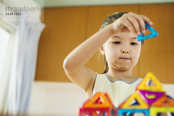 Ein spielendes Mädchen  das eine Struktur mit bunten geometrischen Formen aufbaut.