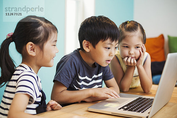 Drei Kinder mit einem Laptop  zwei Mädchen und ein Junge.