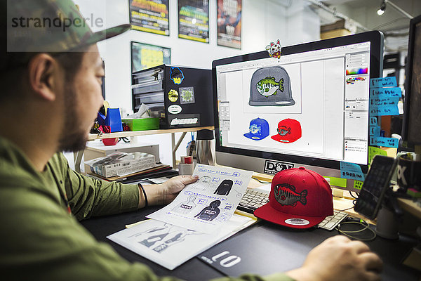 Ein Mann  ein Designer  der am Bildschirm arbeitet und Entwürfe für Baseballcaps entwirft.