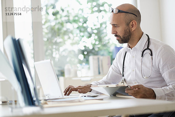Konzentriert arbeitender Arzt mit Laptop am Schreibtisch im Büro