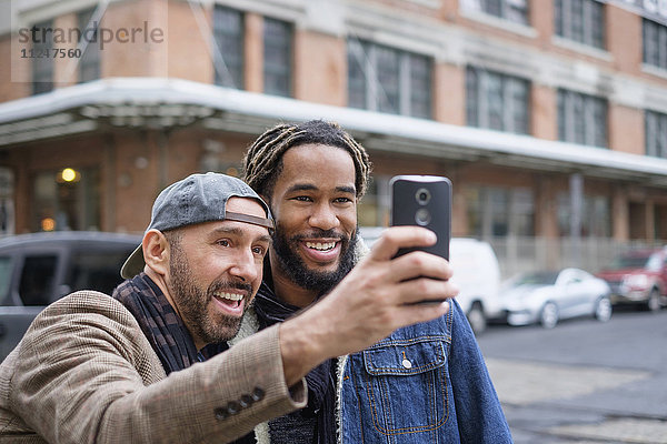 Lächelndes homosexuelles Paar  das ein Selfie mit einem Smartphone auf der Straße macht