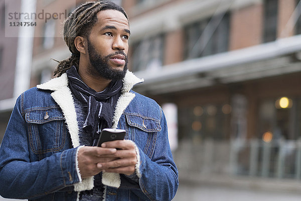 Ernster Mann mit Dreadlocks hält Smartphone auf der Straße
