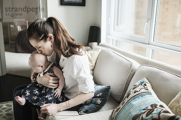 Mutter küsst den Kopf ihrer kleinen Tochter (2-5 Monate) im Wohnzimmer