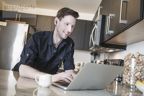 Mann lächelt bei der Arbeit am Laptop in der Küche