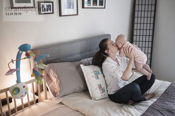 Mutter küsst ihre kleine Tochter (2-5 Monate) im Schlafzimmer