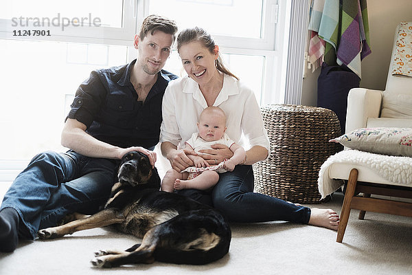 Porträt einer glücklichen Familie auf dem Teppich sitzend mit Tochter (2-5 Monate) und Hund