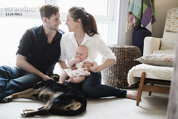 Porträt einer glücklichen Familie auf dem Teppich sitzend mit Tochter (2-5 Monate) und Hund