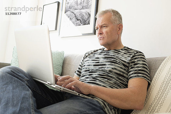 Mann sitzt auf dem Sofa und benutzt einen Laptop