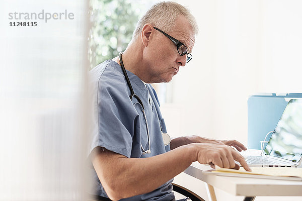 Mann im Kittel benutzt Laptop in einer Arztpraxis