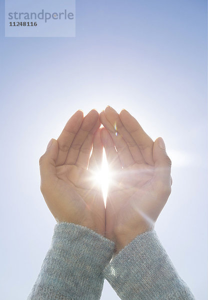 Weibliche Hände vor klarem Himmel  die Sonne scheint durch die Finger