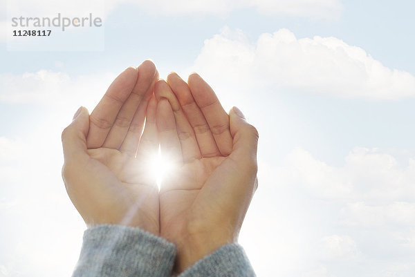 Weibliche Hände gegen Wolken  die Sonne scheint durch die Finger