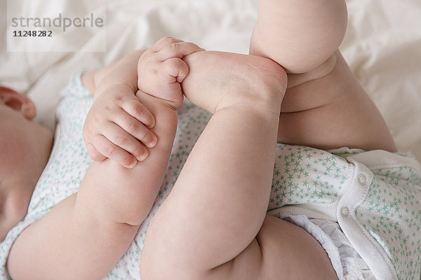 Kleines Mädchen (12-17 Monate) im Liegen mit den Händen auf den Füßen