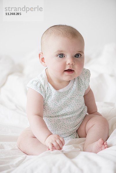 Kleines Mädchen (12-17 Monate) auf dem Bett sitzend