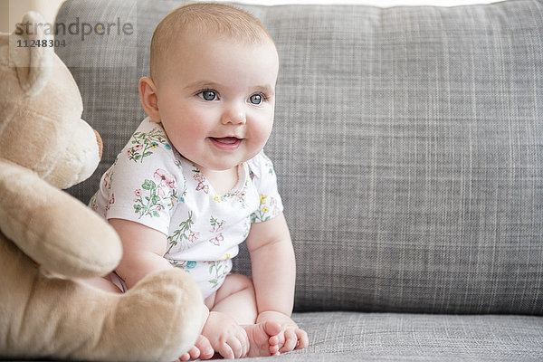 Kleines Mädchen (12-17 Monate) mit Teddybär auf dem Sofa sitzend