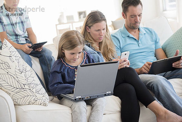 Familie mit zwei Kindern (6-7  8-9) auf dem Sofa sitzend  mit Laptop und digitalen Tablets
