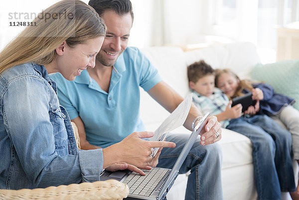 Mann und Frau beim Bezahlen von Rechnungen mit zwei Kindern (6-7  8-9) auf dem Sofa sitzend  mit digitalem Tablet