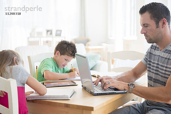 Mann mit Laptop und zwei Kindern (6-7  8-9)  die in Notizblöcke schreiben