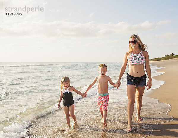 Mutter geht mit Junge (6-7) und Mädchen (4-5) am Strand am Wasser spazieren