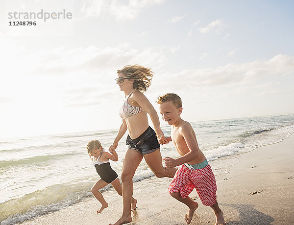 Mutter läuft mit Junge (6-7) und Mädchen (4-5) am Strand am Wasser
