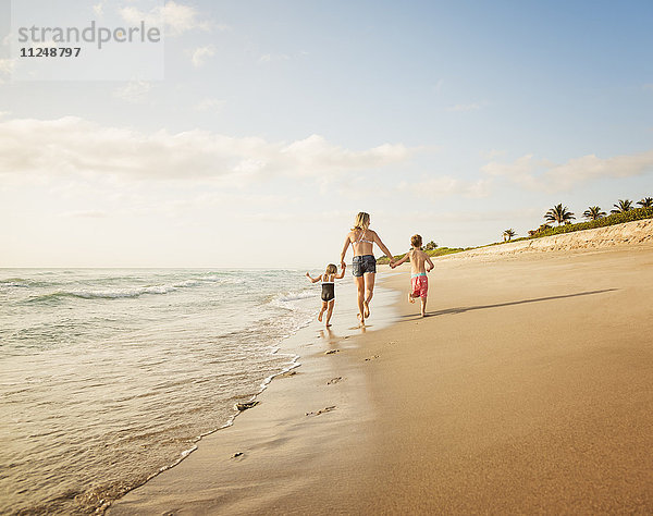 Mutter läuft mit Junge (6-7) und Mädchen (4-5) am Strand am Wasser