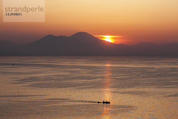 Silhouette eines Bootes auf dem Meer mit Bergen im Hintergrund bei Sonnenuntergang