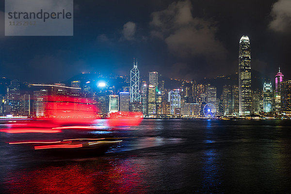 Ein rotes Dschunken-Segelboot gleitet nachts vor der Skyline von Hongkong  Hongkong  China  Asien