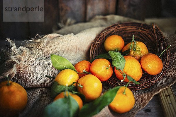 Mandarinen mit Blättern im Korb auf rustikalem Holzuntergrund