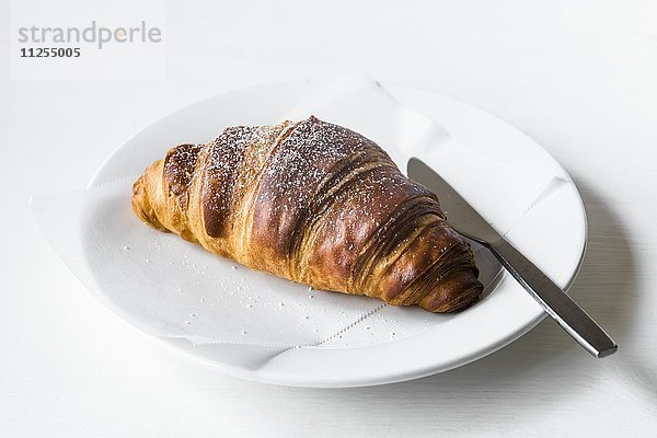 Croissant auf weissem Teller mit Messer