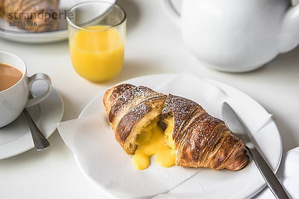 Aufgeschnittenes Croissant  gefüllt mit gesalzenem Eigelb  auf Teller mit Tee und Orangensaft