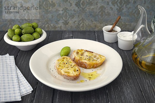 Zwei Baguettescheiben mit Olivenöl und Oliven (Arbosana  Chile)