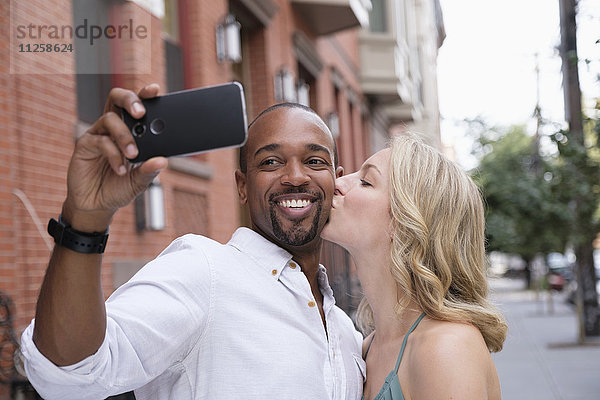 Frau küsst Freund auf die Wange  Mann macht Selfie