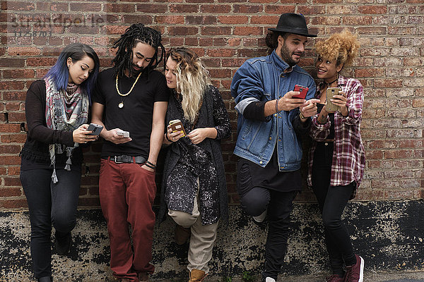 Porträt von Freunden mit Smartphones vor einer Mauer